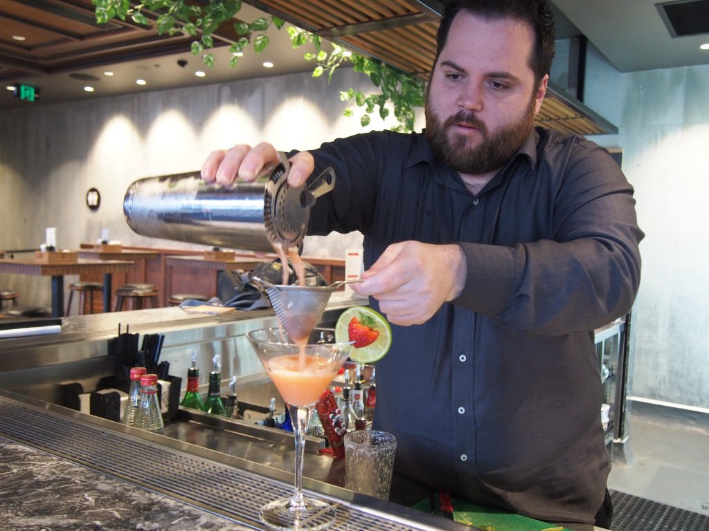 Male bar tender during drink into cocktail glass.