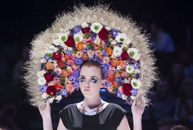 Female model wears a large floral headpiece.