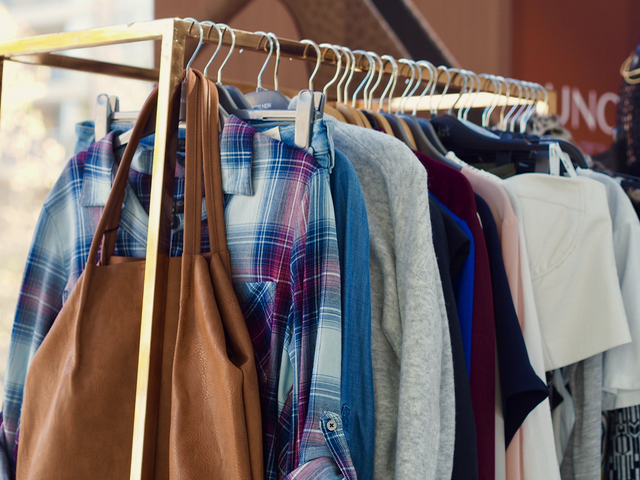 A clothes rack with an assortment of clothes and a brown bag.
