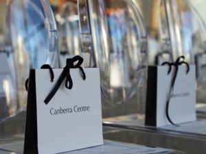 A row of clear chairs with white gift bags on them. The bags say Canberra Centre.
