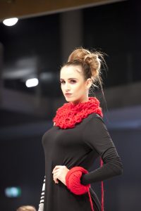 Model wears black dress with red neck lace and bracelet.